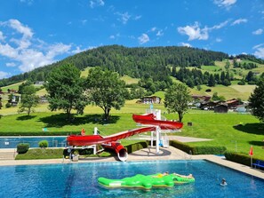 Una piscina con tobogán de agua, rodeada de vegetación y casas.