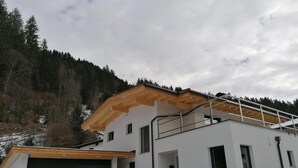 A modern two-story building with a garage, a balcony, and a view of a forested hillside.