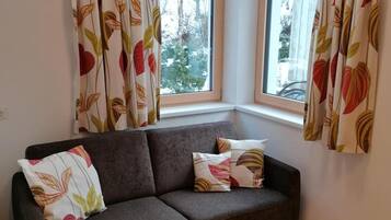 Habitación de esquina con un sofá gris oscuro, dos almohadas y una ventana con cortinas.