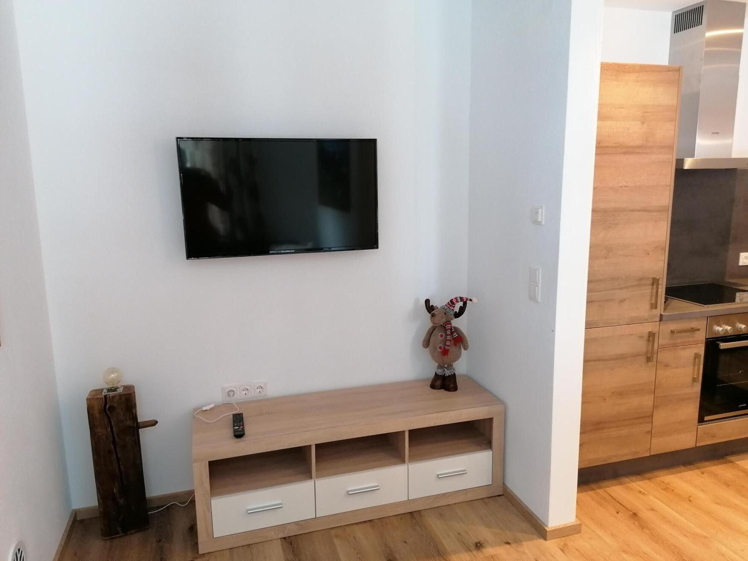A modern kitchen with wooden cabinets, a built-in oven, and a television mounted on the wall.