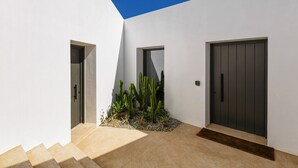 Um edifício moderno com fachada branca, porta escura e um pequeno jardim de cactos em frente.