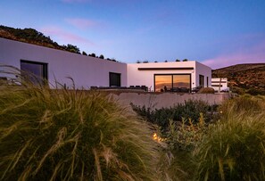 A modern house with a flat roof, large windows, and a view of the surrounding landscape. - Paros Villa Skylines Estate II (Paros)