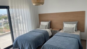 Una camera da letto moderna con due letti, un'ampia finestra e vista sulla città.