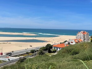 A coastal view with a beach, a road with vehicles, and a building with a red roof. - Casa Céu Azul - Gorgeous 3-bedroom villa in charming Nadadouro (Nadadouro)