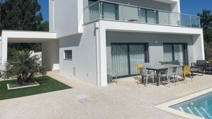 Una moderna casa a due piani con un balcone, una piscina e area salotto esterna.