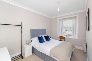 Ein Schlafzimmer mit Bett, Nachttisch, Fenster und Heizkörper.