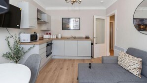 A compact living space with a kitchenette, a grey sofa, a small dining table, and a chandelier.