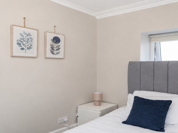 A bedroom with a bed, a bedside table, a lamp, and two framed wall art pieces.