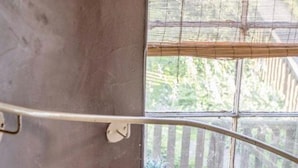 A concrete staircase with a metal handrail leading to a window overlooking greenery.