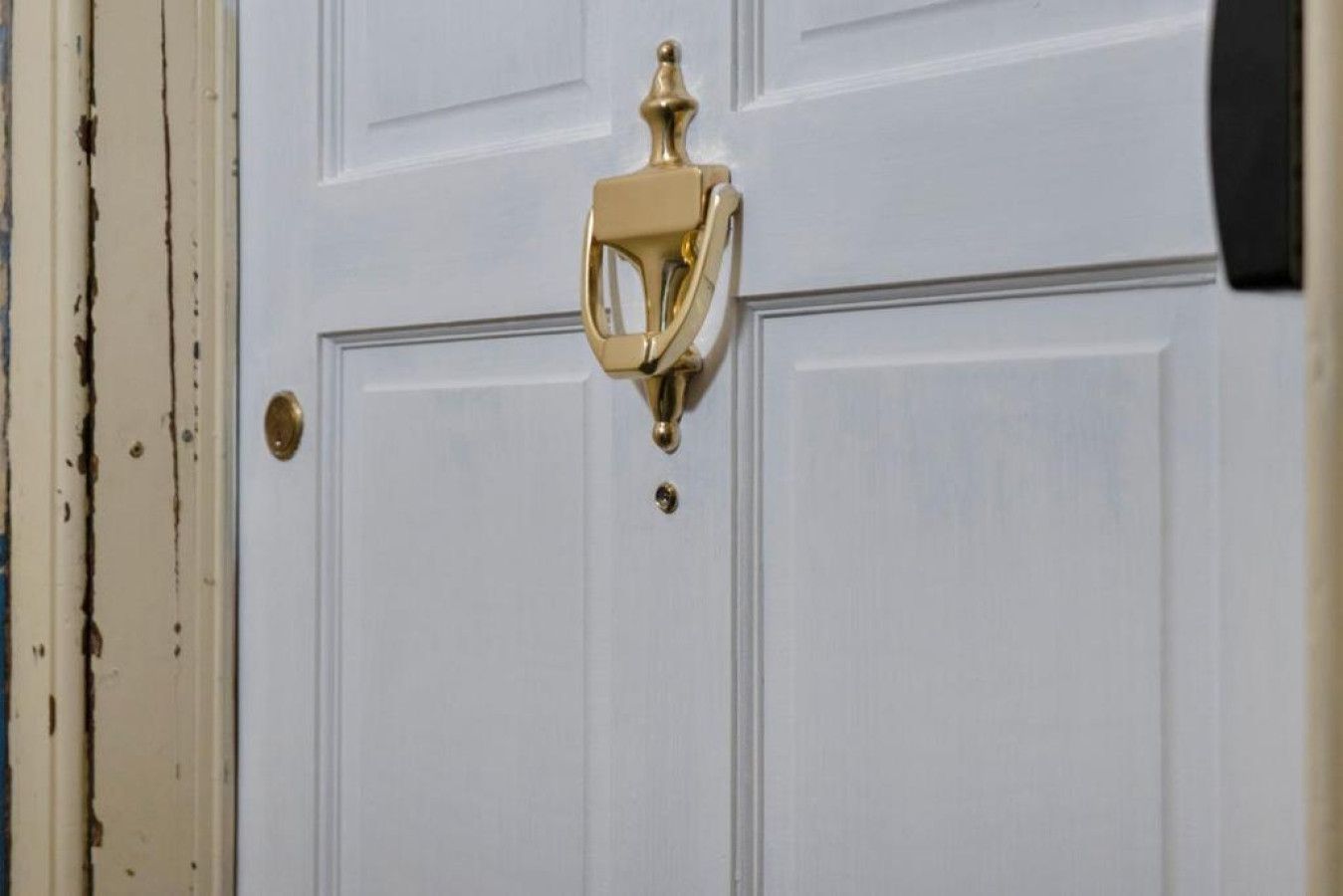 Una puerta blanca con un llamador de latón.