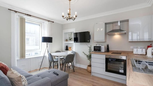 A modern kitchen with white cabinets, a dining area with a table and chairs, a sofa, and a chandelier.