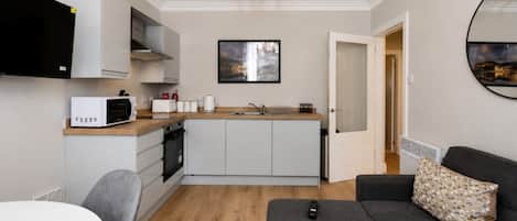 Un espacio habitable compacto con kitchenette, comedor y zona de estar con sofá y mesa.