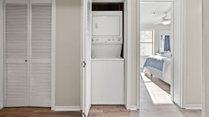 Une buanderie équipée d’un lave-linge et d’un sèche-linge, un placard avec des portes à persiennes et une chambre à coucher avec un lit et une fenêtre.