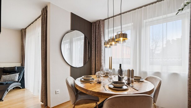 A dining area with a round table set for four, a large mirror, and a view of the city through large windows. - Luxurious apartment I Fully equipped I University within walking distance (Homburg)