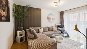 A modern living room with a sofa, a coffee table, a potted plant, and a large window with curtains. - Luxurious apartment I Fully equipped I University within walking distance (Homburg)