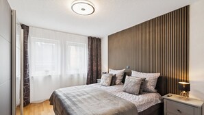 A modern bedroom with a large bed, a bedside table with a lamp, and a wall with vertical wooden slats. - Luxurious apartment I Fully equipped I University within walking distance (Homburg)
