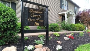A sign for Lancaster County Guest House with a garden in front. - Forget your worries and enjoy some peace in the beautiful Lancaster Guest House. (New Holland)