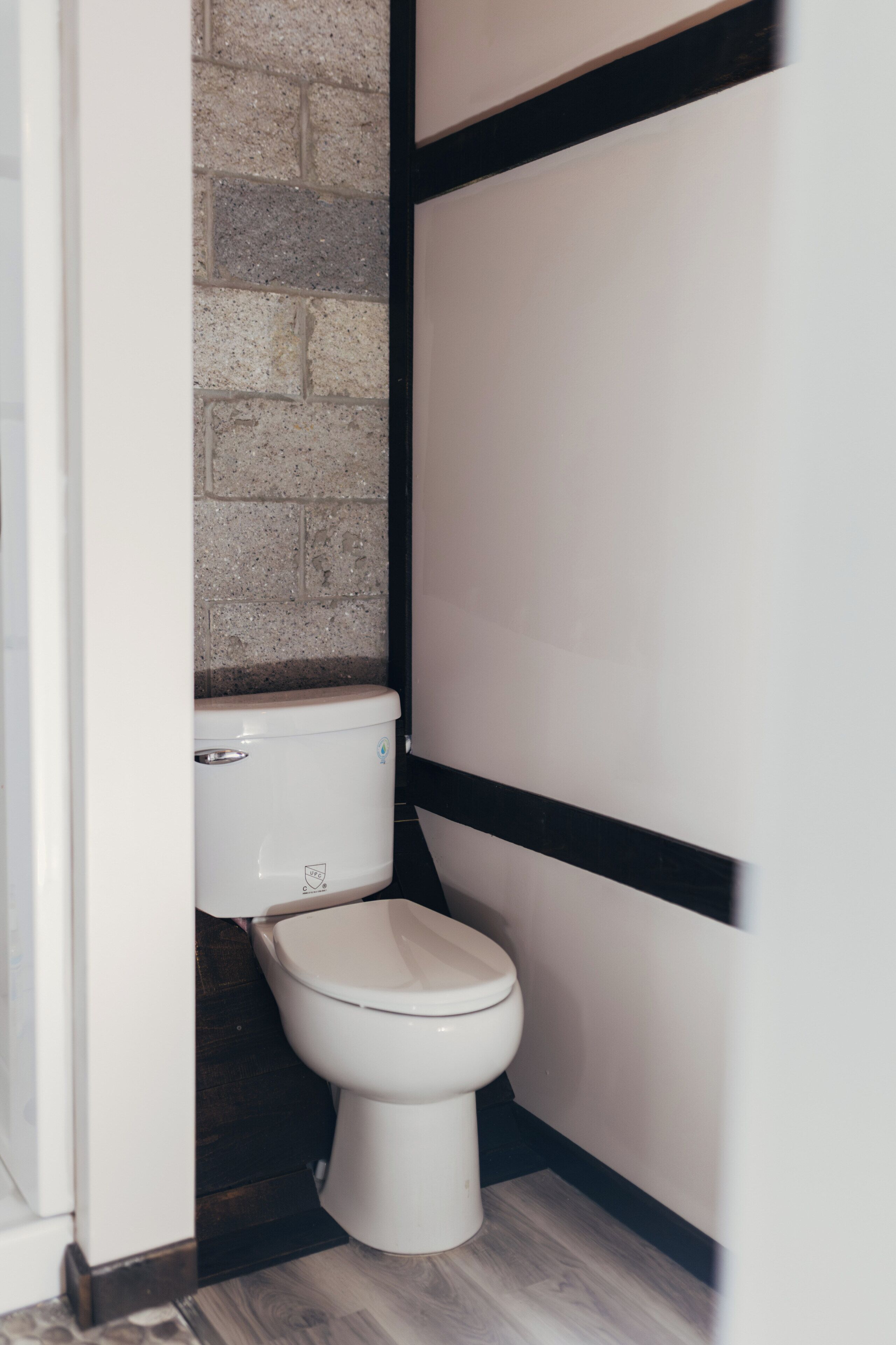 A compact bathroom with a white toilet, a brick wall, and a black and white panel design.
