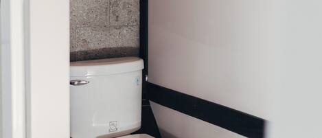 A compact bathroom with a white toilet, a brick wall, and a black and white panel design.