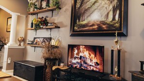 A living room with a fireplace, a mounted TV, and a framed forest painting. - Forget your worries and enjoy some peace in the beautiful Lancaster Guest House. (New Holland)