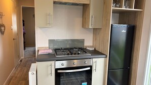 A compact kitchen with a gas stove, oven, and a black refrigerator. - M&B Holiday,Cozy Beach side Caravan 4 Beds, 3 Sofa Bed, 7 Sleep,Wifi&Tea,Parking (Saint Osyth)