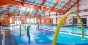 An indoor swimming pool with colorful water slides and a high ceiling with orange beams.