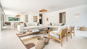 Ein modernes Wohnzimmer mit einer Couch, einem Couchtisch und Sesseln. Im Hintergrund ist ein Essbereich mit Tisch und Stühlen zu sehen.