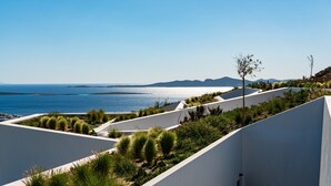 A modern architectural design with white walls and green landscaping, overlooking a coastal area with a clear view of the sea and distant mountains. - Paros Villa Skylines Estate III (Paros)