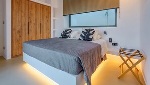 A modern bedroom with a large bed, wooden wardrobe, and a unique wall-mounted mirror. - Paros Villa Skylines Estate III (Paros)