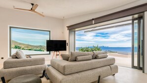 A modern living room with a large sofa set, a flat-screen TV, and a stone accent piece. - Paros Villa Skylines Estate III (Paros)