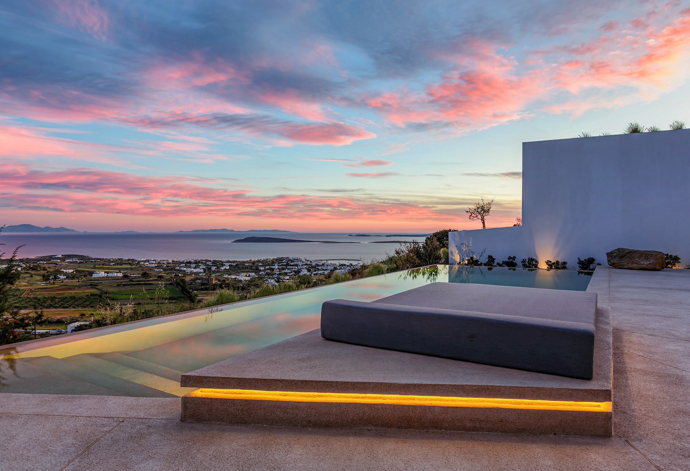 Ein moderner Poolbereich im Freien mit Blick auf das Meer und die ferne Landschaft bei Sonnenuntergang.
