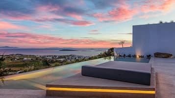 Ein moderner Poolbereich im Freien mit Blick auf das Meer und die ferne Landschaft bei Sonnenuntergang.