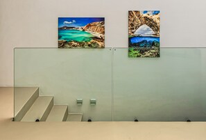 Eine Treppe mit Glastrennwand und zwei gerahmten Fotografien von Küstenlandschaften.