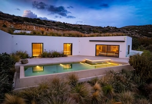 Ett modernt hus med en swimmingpool, stora fönster och utsikt över det omgivande landskapet.