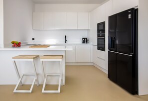 Cozinha moderna com armários brancos, geladeira preta e dois banquinhos de madeira.