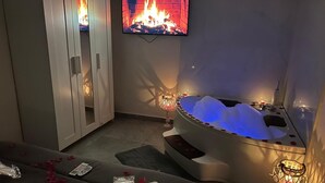A spa room with a bathtub, a television displaying a fireplace, and rose petals scattered on the floor. - B&b HOUSE NAPLES CAPODICHINO (Napoli)