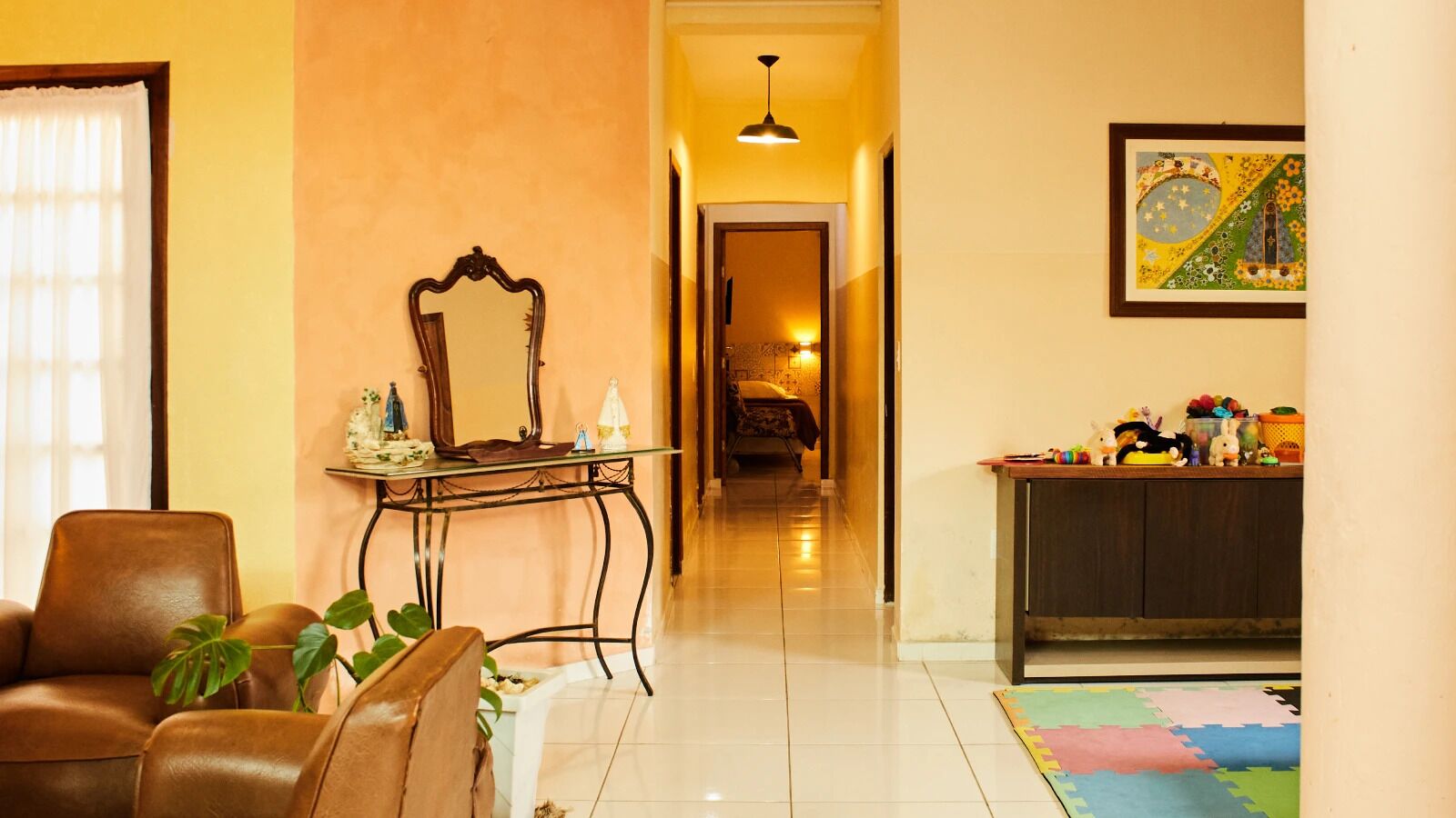 A hotel lobby with a brown leather chair, a small table with a mirror, a colorful rug, and a framed artwork on the wall.