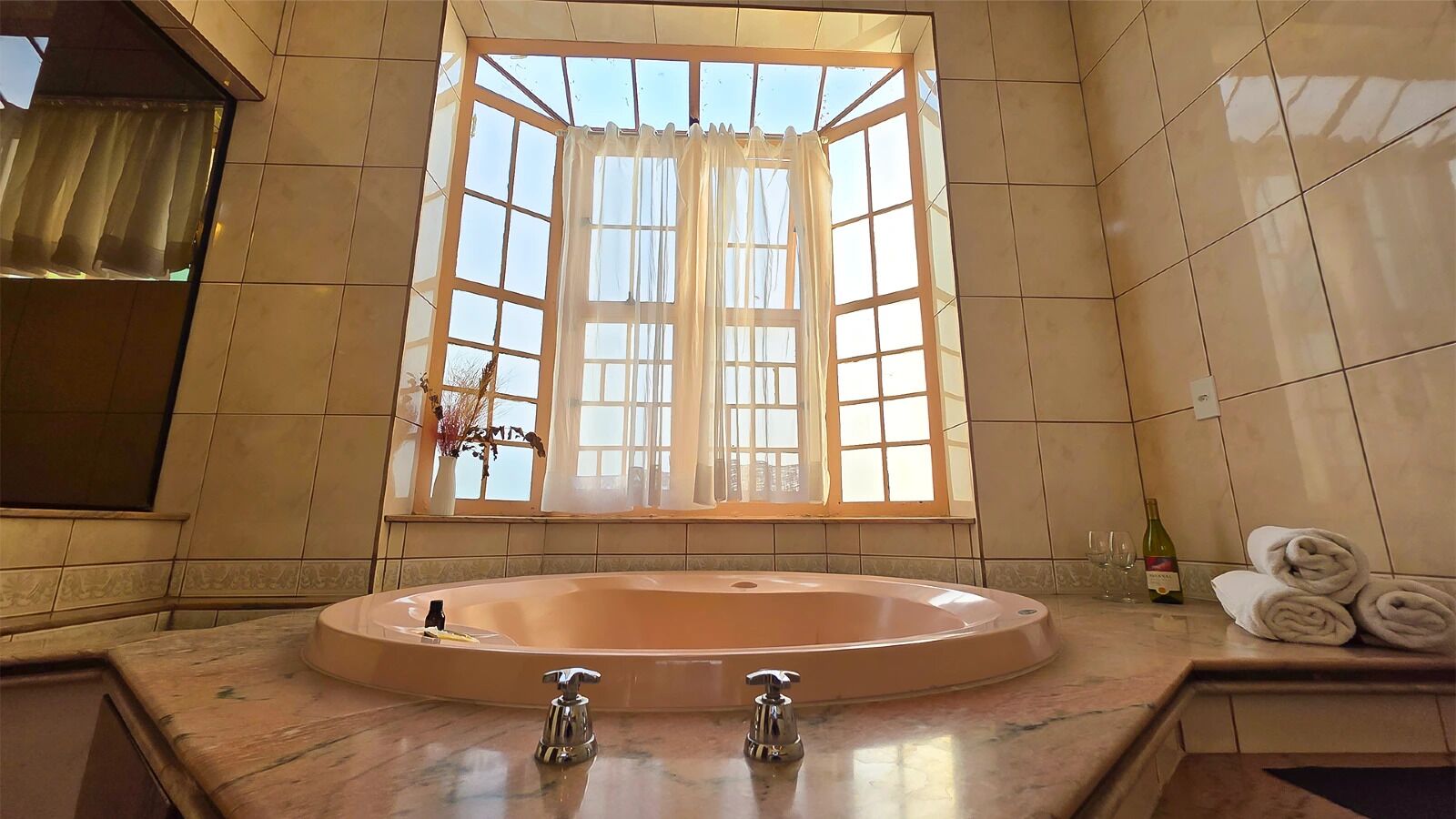Un baño con una bañera ovalada grande, una ventana con cortinas y una pared de azulejos.