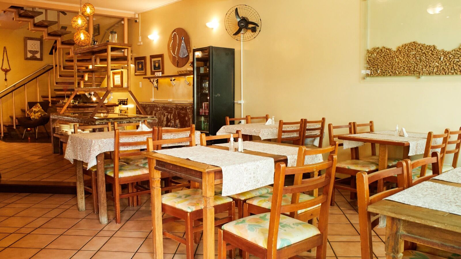 A restaurant with wooden tables and chairs, a staircase, and a fan on the wall.
