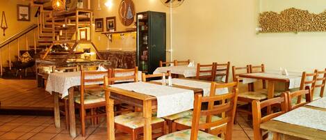 A restaurant with wooden tables and chairs, a staircase, and a fan on the wall.