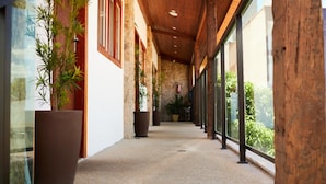 Um corredor com plantas em vasos, paredes de pedra e grandes janelas.