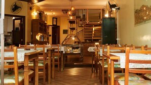Um restaurante acolhedor com mesas e cadeiras de madeira, uma escada e um ventilador na parede.