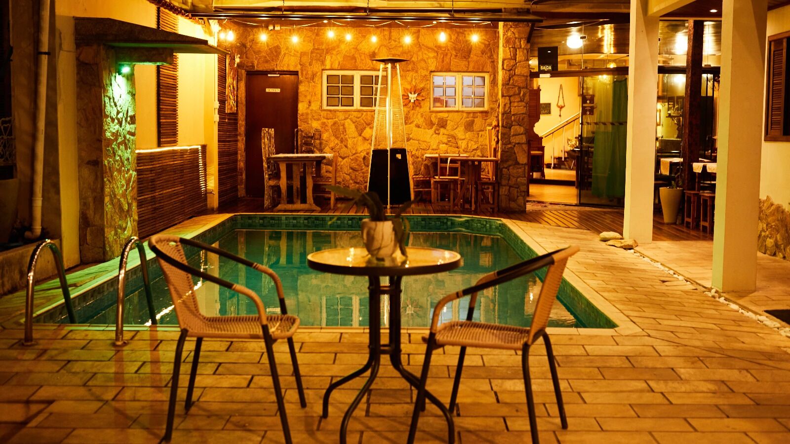 An indoor pool area with a stone wall, a table with chairs, and a staircase leading to an upper level.