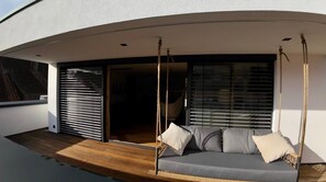 A modern outdoor seating area with a swing chair and cushions, a wooden deck, and a sliding glass door leading to an interior space.