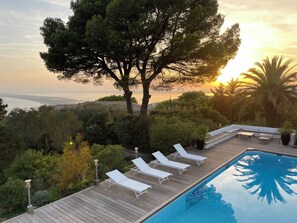 Un espace aménagé au bord de la piscine, avec des chaises longues et une vue sur le coucher de soleil en mer.