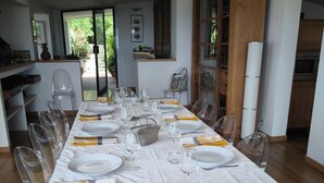 A dining area with a long table set for a meal, clear chairs, and a view of the outdoors.