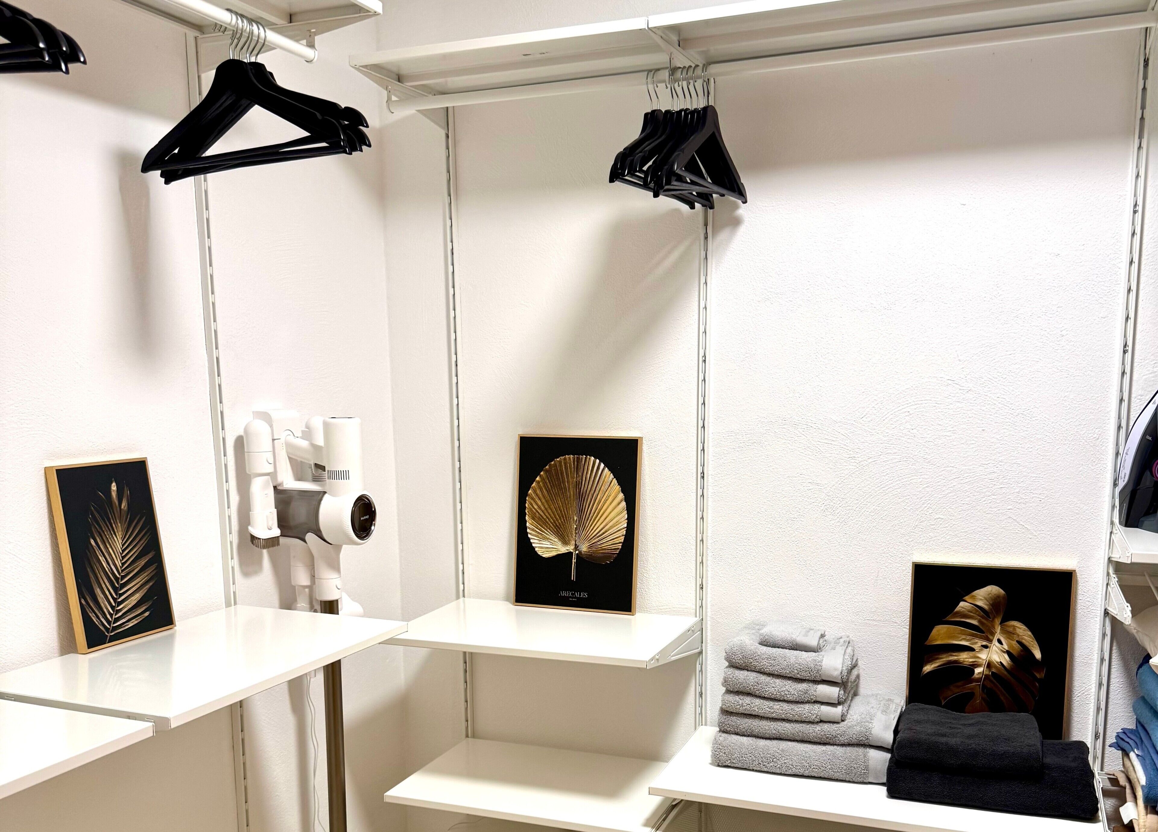 Une salle de bain avec un meuble-lavabo blanc, un sèche-cheveux, une œuvre d’art représentant une feuille encadrée et des serviettes.