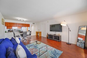 A modern living room with a blue sofa, a coffee table, a flat-screen TV, and a kitchen in the background. - Brickell Bay 1720 (Miami)