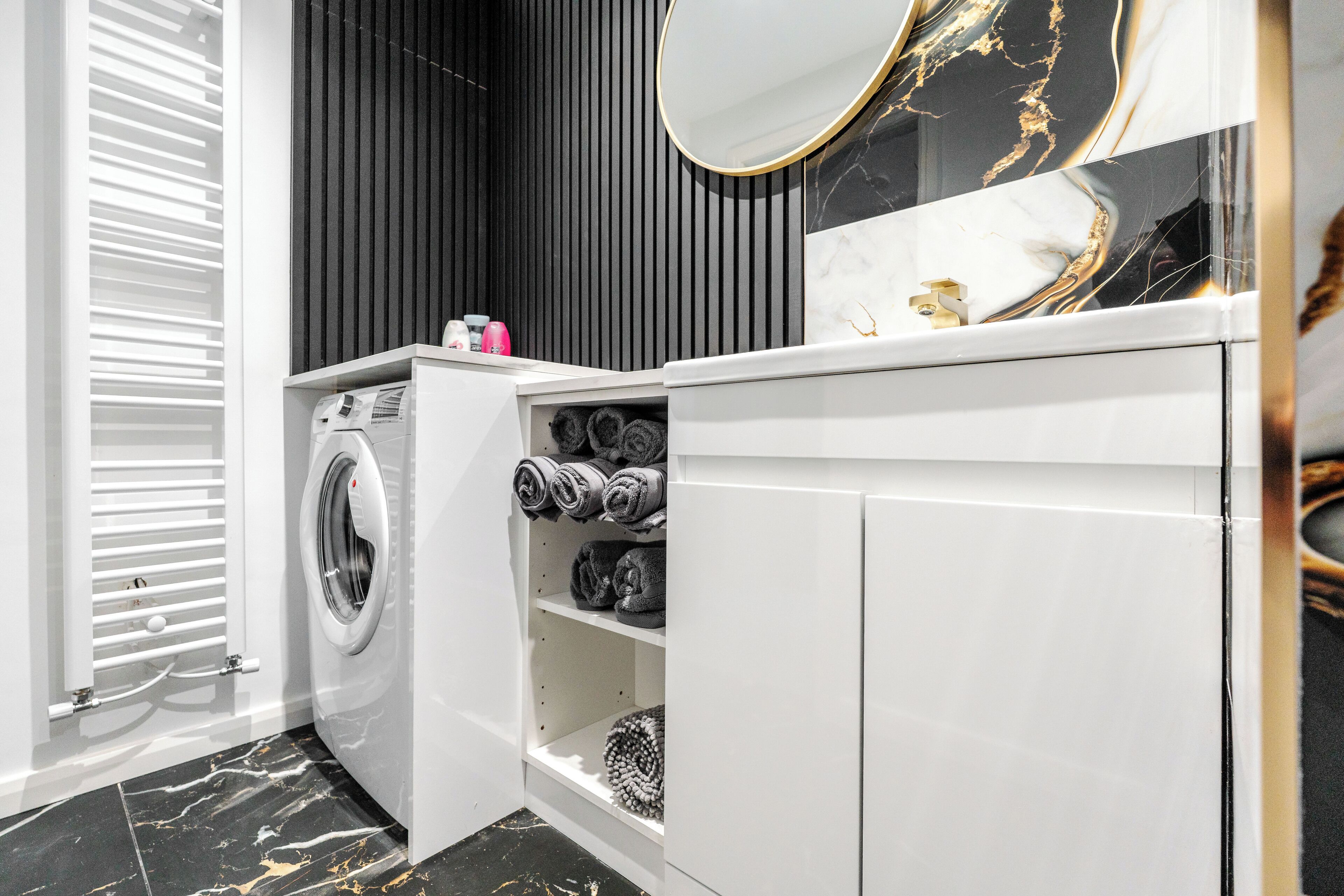 A modern bathroom with a built-in washing machine, a vanity with a mirror, and shelves for towels.