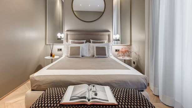 A modern hotel room with a large bed, a round mirror, and a book on the bed. - BDC - LuxuryLifeStyle (Roma)